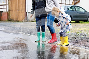 Close-up of three children, toddler girl and two kids boys wearing red, yellow and green rain boots and walking during