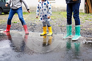 Close-up of three children, toddler girl and two kids boys wearing red, yellow and green rain boots and walking during