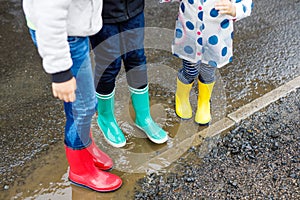 Close-up of three children, toddler girl and two kids boys wearing red, yellow and green rain boots and walking during