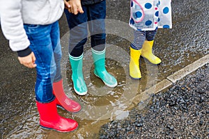 Close-up of three children, toddler girl and two kids boys wearing red, yellow and green rain boots and walking during