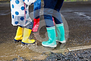 Close-up of three children, toddler girl and two kids boys wearing red, yellow and green rain boots and walking during