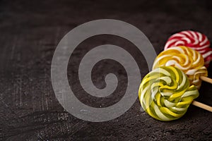 Close-up of a three colorful caramels on a stick arranged in a diagonal row on a dark metallic background. Copy space