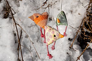 Close-up of three funny colorful chickens made of fabric hanging on a branch with a snow background photo