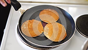 Close-up of three golden ruddy pancakes in a frying pan, light white steam.