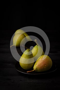 Close up of three green pears on black plate, with two more in the background, selective focus, black background,