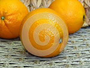 Close up of three juicy orange yellow oranges on rattan cane bamboo handmade woven works background.