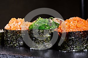 Close up of three pieces of sushi with different fillings on a black plate.