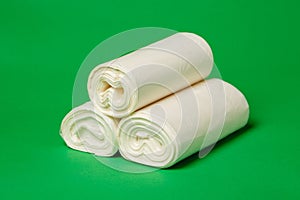 Close up of three rolls of white environmental garbage bags on green background.