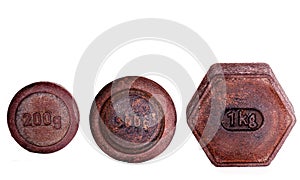 Close up of three rusty standard metric weights made of iron for weighing scales on white background.