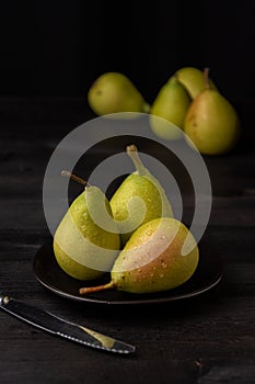 Close-up of three wet green pears on black plate, with four more in the background, selective focus