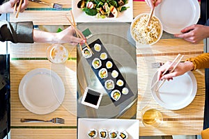 Food detail concept. Three women eating sushi and yakisoba with chopsticks in the restaurant.