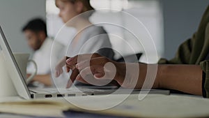 Close-up of three young adults in businesswear working on laptops at desk in office