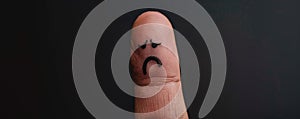 Close-up of a thumb with a sad face drawing on black background