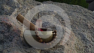 Close-up, Tibetan singing bowl and runes stand on a huge stone, incense smokes nearby