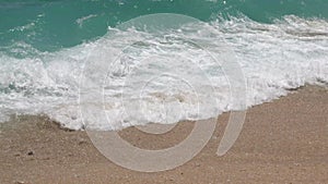 Close up tide waves with foam and splashes in sunny day in ocean on tropic white sand beach. Water surface texture and