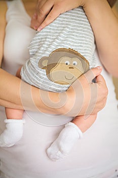 Close-up of tiny baby in socks in the hands of his mother. Young mom hugging her newborn child. Motherhood and childhood