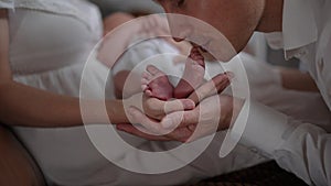 Close-up tiny newborn baby feet in female hand with happy man kissing little toes in slow motion smiling. Excited