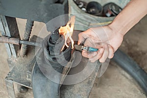 Close up of tire repairman`s hand when starting a fire with a lighter on a traditional press photo