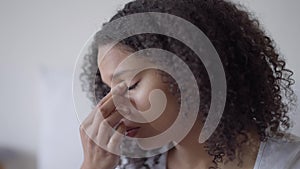 Close-up of tired beautiful African American woman rubbing eyes working at home office indoors. Headshot portrait of