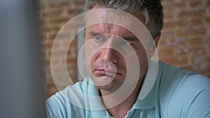 Close-up tired face of adult caucasian businessman looking at the screen of computer and trying to concentrate, business