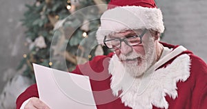Close-up of tired Santa Claus in eyeglasses scratching his head as reading letter. Old man thinking on gift for child on