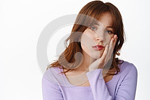 Close up of tired young girl with freckles and bangs, lean face on hand, staring reluctant and uninterested, looking photo