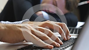 Close up to arms of young manager typing text on laptop keyboard at office. Male hands of businessman working on