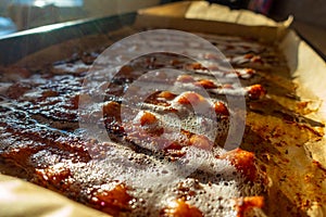 Close up to bacon cooking on a cookie sheet with foam bubbling on top