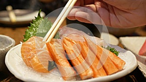 close up to a bowl of sashimi fresh raw fish japanese food while using chopsticks to pick salmon sashimi from bowl on ice to eat