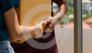 Close up to hand of young asian couple when they carrying big cardboard box while relocation into new home on moving day,