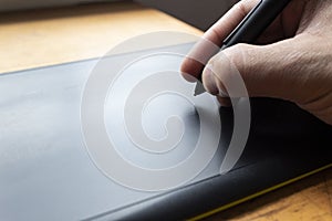 Close up to a male hand holding up a black digital pencil over a black and green drawing tablet in desk and home office background