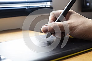 Close up to a male hand holding up a black digital pencil over a black and green drawing tablet in desk and home office background