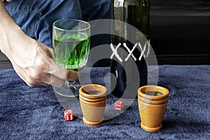 Close up to a man holding a cup of green homemade liquor with two wooden cups and green artesanal alcohol bottle and dices photo