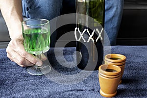 Close up to a man holding a cup of green homemade liquor with two wooden cups and green artesanal bottle photo