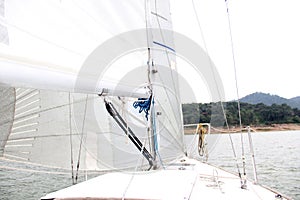 Close up to parts of a sailboat that is sailing: mast, mainsail, sheet, rudder, bow, stern, weather vane, boom, jib