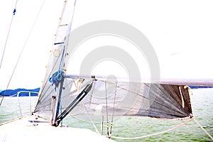 Close up to parts of a sailboat that is sailing: mast, mainsail, sheet, rudder, bow, stern, weather vane, boom, jib