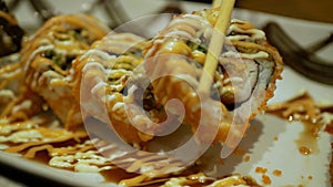 close up to a plate of futomaki sushi with fresh raw fish japanese food while using chopsticks to pick sushi from plate to eat