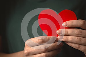 Close-up to red heart in hands. Woman holding paper heart on her chest background