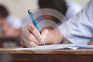 Close-up to student holding pen and writing final exam in examination room or study in classroom