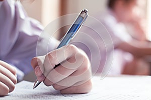 Close-up to student holding pencil and writing final exam in examination room or study in classroom