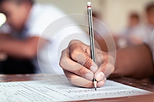 Close-up to student holding pencil and writing final exam in examination room or study in classroom