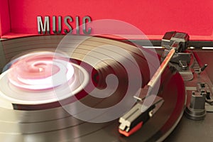 Close up to a turn table needle playing a LP vinyl disc with turn table and MUSIC lettering word over red background