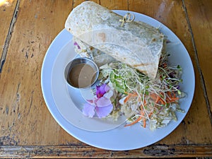 Close-up of Tofu Burrito that been cut in half with salad, dressing, and flower on a plate