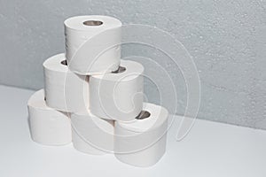 Close-up of toilet paper rolls on white table with background of textured grey wall.