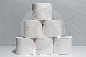 Close-up of toilet paper rolls on white table, background of textured wall grey of color.