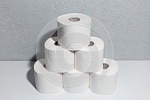 Close-up of toilet paper rolls on white table, background of textured wall grey of color.