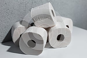 Close-up of toilet paper rolls on white table, background of textured wall grey of color.