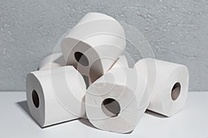 Close-up of toilet paper rolls on white table, background of textured wall grey of color.