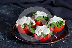 Close - up of tomato halves with finely chopped parsley in a sauce of sour cream and salt lie on a plate on a dark