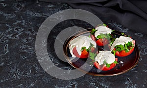 Close - up of tomato halves with finely chopped parsley in a sauce of sour cream and salt lie on a plate on a dark